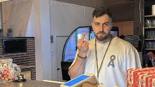 Inhaber Serdar Bingöl steht hinter dem Tresen und zeigt einen Stinkefinger