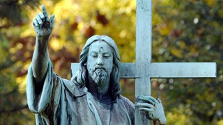 eine Jesus-Statue mit Kreuz am Rande eines Friedhofs