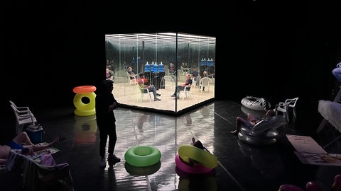 Ein Glaskasten im dunklen Theaterraum.