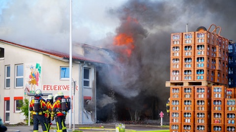 Feuerwehrleute stehen vor dem brennenden Gerätehaus der Feuerwehr Unterensingen.