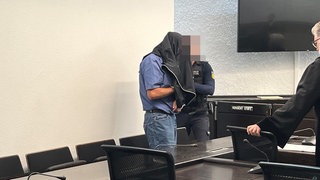 Ehemaliger Tagesvater verdeckt sein Gesicht mit einem Kleidungsstück bei Prozess wegen Kindesmissbrauch im Landgericht Stuttgart.