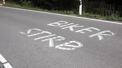 Auf einer Straße ist der Schriftzug "Biker stirb!" zu sehen.
