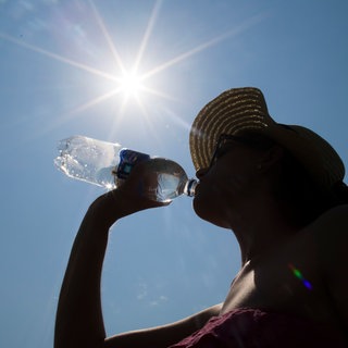 Eine Frau mit Sonnenhut trinkt unter der Mittagssonne aus einer Wasserflasche: Mineralwasser ist angesichts der Hitze derzeit starkt gefragt in Baden-Württemberg.