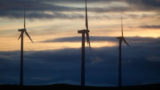 Drei Windräder vor Himmel und dunklen Wolken.