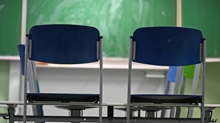 Zwei leere Stühle stehen in einem Klassenraum vor einer Tafel. Pisa-Studie: Deutsche Ergebnisse so schlecht wie nie.