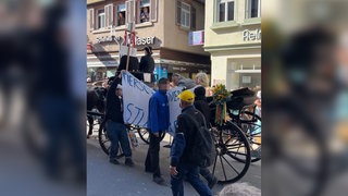Zwei Aktivisten mit einem Transparent beim Volksfestumzug in Stuttgart 2026
