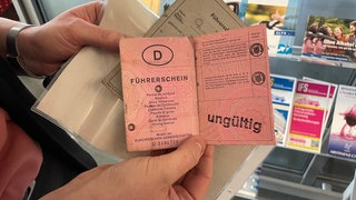 Eine Frau hält einen alten, rosanen Führerschein, der inzwischen ungültig ist. Beim Umtausch zu einem neuen Führerschein im Scheckkartenformat können manche Menschen mit Behinderung Schwierigkeiten bekommen und ein Gutachten benötigen.