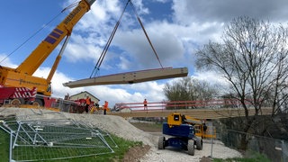 Mit einem Kran wird ein Brückenteil an seinen Standort gebracht. In wenigen Monaten wird aus der Baustelle eine Neckarbrücke.
