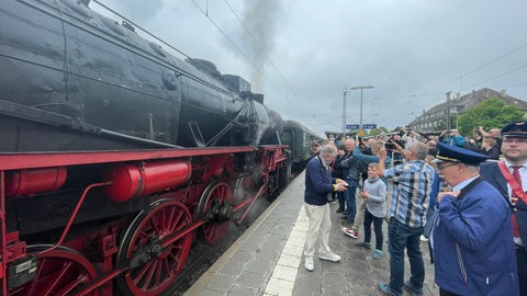 Die Dampflok Liesel der Eisenbahnfreunde Zollernalb steht dampfend auf den Gleisen, viele Menschen am Bahnsteig machen Fotos und Videos.