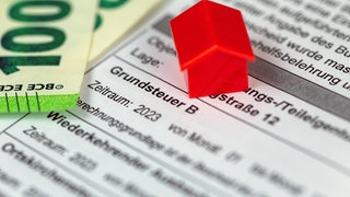 Ein Spielzeughaus steht auf Grundsteuerunterlagen. Verwaltung und Gemeinderat der Stadt Tübingen wollen Steuererhöhungen durchsetzen.