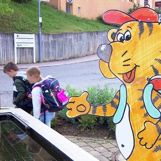 Zwei Kinder laufen an einem Tiger-Schild vorbei. Die Grundschule Bodelshausen hat sich was gegen Elterntaxis überlegt.