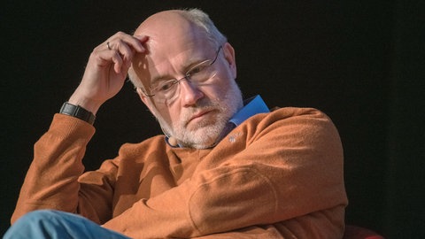 Harald Lesch nachdenklich bei einer Podiumsdiskussion: Bei der Tübinger Mediendozentur will er über die Folgen gezielter Falsch-Informationen sprechen.