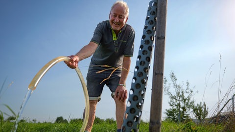 Joachim Funk vom Obst- und Gartenbauverein Mössingen hält Schlauch auf die jungen Obstbäume. Er versorgt sie bei der Hitze mit Wasser.