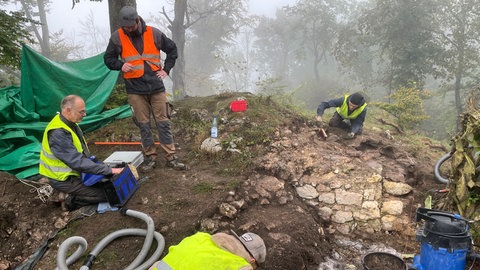 Im nebligen Wald werden Überreste einer Mauer freigelegt. Studierende und Mitarbeitende der Uni Tübingen beginnen mit den Ausgrabungen an der Burg Hohengenkingen.