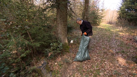 Ein Mann sammelt in einen großen Müllsack den Dreck ein, den andere liegen gelassen haben
