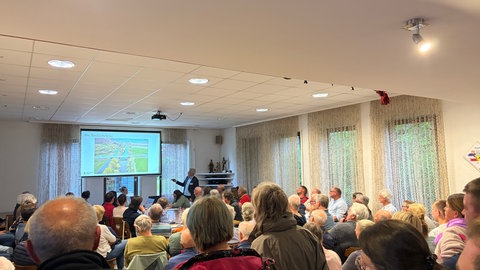 Ein Mann vom Regierungspräsidium erklärt mit einer Präsentation den aktuellen Stand beim geplanten Neubau der maroden Hirschauer Brücke.