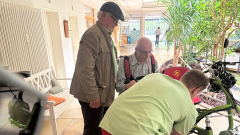 Eberhard Kocher steht neben Pflegefachkraft Konrad Loges, der Thomas Lipp auf seine Fahrt mit der Rikscha vorbereitet. Die Rikscha-Tour ist für die Mössinger Pflegeheimbewohner kostenlos. 