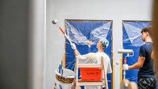 Zwei Menschen mit Malerrollen nd abgeklebten Wänden. Schüler des Eugen-Bolz-Gymnasiums streichen die Schulwände, nachdem im Sommer 2025 ihr Abistreich missglückt ist (Archiv).