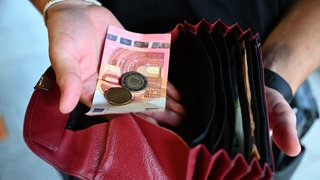 Jemand hält einen Geldbeutel in der Hand, während er in der anderen Hand Geld hält. Die Uniklinik Tübingen hat herausgefunden: Zahlen mit Bargeld kann schmerzen auslösen.