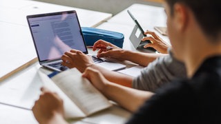 Schüler eines Gymnasiums sitzen vor einem Computer und benutzen ein KI-Tool. Jeder dritte befragte Jugendliche hält KI für klüger als die eigenen Lehrer.
