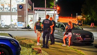 Einsatzkräfte der Polizei stehen am Tatort an einer Straße.