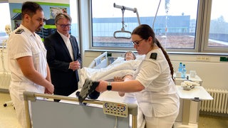 Der baden-württembergische Sozialminister Manfred Lucha (Grüne) lässt sich am Bundeswehrkrankenhaus in Ulm zeigen, was eine künftige Krankenschwester lernen muss. Im Bett liegt eine Puppe.