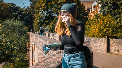 Eine junge Frau lehnt an der Ulmer Stadtmauer und bläst Seifenblasen in die Luft. Eine Hand steckt in einer Handorthese. Hergestellt hat sie ein Unternehmen aus Ulm - für Menschen, deren Hände gelähmt sind.