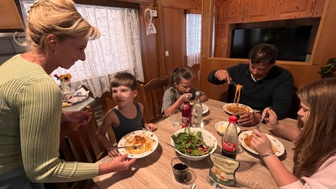 Die Zirkusfamilie BöhmMendesHeppenheimer sitzt beim Mittagessen um den gemeinsamen Tisch im Wohnwagen