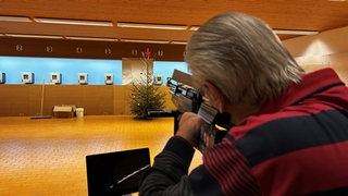 Ein Mann schießt mit einem Luftgewehr auf eine Christbaumkugel, die an einem Weihnachtsbaum  hängt. Seit 30 Jahren startet der Schützenverein Hubertus in Illerkirchberg-Beutelreusch mit dem Christbaumkugelschießen in sein neues Trainingsjahr.
