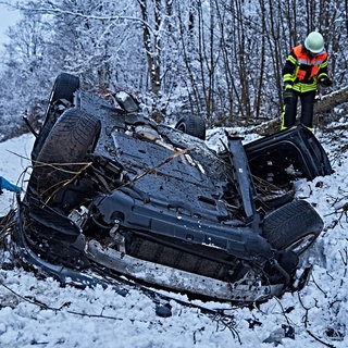 In winterlicher Landschaft liegt ein Auto im Straßengraben auf dem Dach. Feuerwehrleute sind vor Ort. 