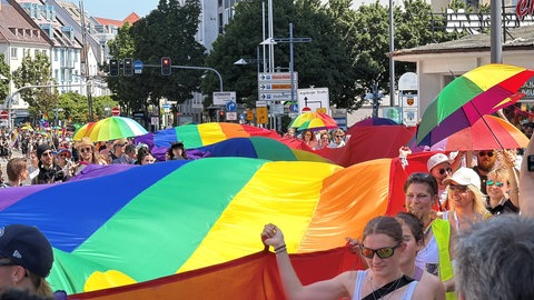 Die Regenbogenfahne wird von zahlreichen Teilnehmenden des CSD in Ulm durch die Straßen getragen. 