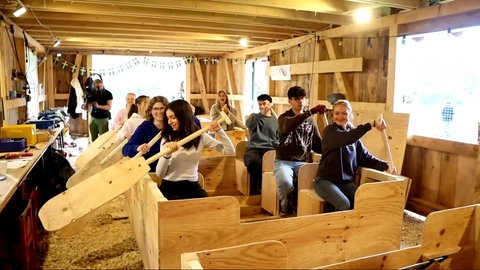 Die Schülerinnen und Schüler sitzen in einer Ulmer Schachtel und halten ihre Paddel in der Hand. Sie haben das Boot selbst gebaut