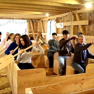 Die Schülerinnen und Schüler sitzen in einer Ulmer Schachtel und halten ihre Paddel in der Hand. Sie haben das Boot selbst gebaut