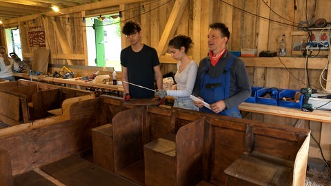 Der Physiklehrer steht mit einem Schüler und einer Schülerin am Boot und bespricht den nächsten Bauschritt.