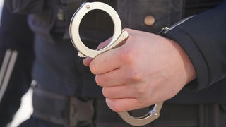 Ein Polizist hält Handschellen in der Hand. Ein 38-Jähriger wurde kurz nach seiner Einreise festgenommen.