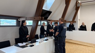 Einem Mann werden im Gerichtssaal die Handschellen abgenommen: Ein Mann muss für vier Jahre in Haft, weil er seinen Arbeitgeber, das Unternehmen Müller, um Millionen Euro betrogen hat. 