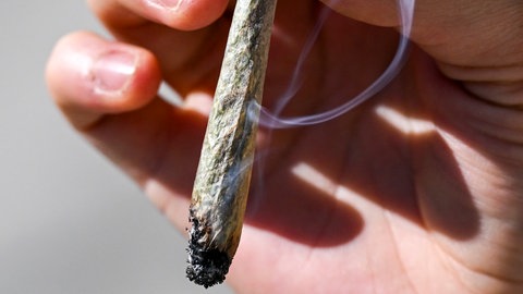 Ein qualmender Joint in einer Hand. Nicht alles, was in einem Hanfladen in der Innenstadt verkauft wurde, war laut Stadt Heidenheim legal (Symbolbild).