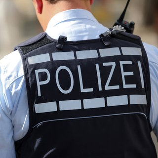 Ein Polizeibeamter trägt eine Weste. Auf dieser steht auf seinem Rücken groß "Polizei". 