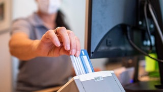 Eine Person schiebt eine Versichertenkarte einer Krankenkasse in eine Lesegerät. Elektronische Rezepte und digitale Patientenakten sollen nach jahrelangen Verzögerungen auf breiter Front zum Einsatz kommen.