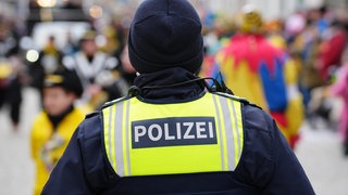 Polizist steht zum Schutz vor einem Fastnachtsumzug mit verkleideten Menschen
