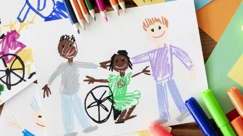Eine Kinderzeichnung zeigt drei Kinder, die einander die Hände auf die Schultern legen. Eines der gezeichneten Kinder sitzt in einem Rollstuhl. Das Bild steht symbolisch für das Thema Inklusion in Kitas und Schulen.
