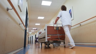 Ein Pfleger schiebt ein Bett in einem Krankenhausflur. Der rheinland-pfälzische Gesundheitsminister Hoch (SPD) hat am Donnerstag den Fahrplan für die Umsetzung der Krankenhausreform vorgestellt. 