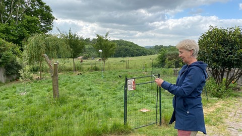 Eine Frau steht auf dem Land und schaut auf ihr Handy. (Bürger und Bürgerinnen wie Claudia Diesler aus Münstermaifeld-Mörz (Kreis Mayen-Koblenz) müssen nach Mobilfunkempfang in ihrem Ort lang suchen.)