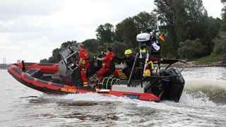 Ein dreiköpfiges DLRG-Team im Einsatzboot fährt über den Rhein - die Kosten zahlt immer wieder die Allgemeinheit.