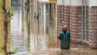 Ein Mann steht im Wasser einer überfluteten Straße. Kommt es in Rheinland-Pfalz zu einem Jahrhunderthochwasser, wären rund 36.000 Wohnadressen betroffen, so die Deutsche Umwelthilfe.