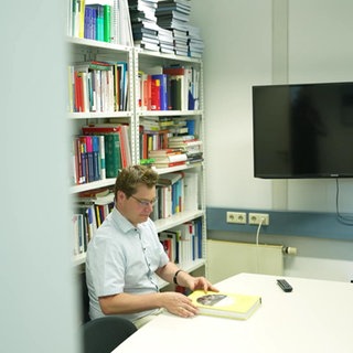 Männliche Person mit einem gelben Buch in einem Büro mit Buchregal