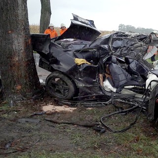 Ein zerstörtes schwarzes Auto steht nach einem Unfall von Fahranfängern neben einem Baum (Symbolbild).