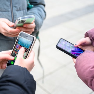 Drei Schüler stehen mit ihren Handys im Pausenhof. Schulen sollen künftig klare Regeln erstellen, wo Smartphones und Co. benutzt werden dürfen.  