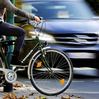 Ein Radfahrer wartet an einer Ampel, ein Auto fährt vorbei (Symbolbild). In RLP kommt es im Straßenverkehr offenbar immer öfter zum Streit zwischen Autofahrern und Radfahrern.