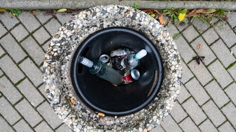 Blick aus der Vogelperspektive in einen öffentlichen Mülleimer, in dem leere Wein- und Schnapsflaschen liegen.